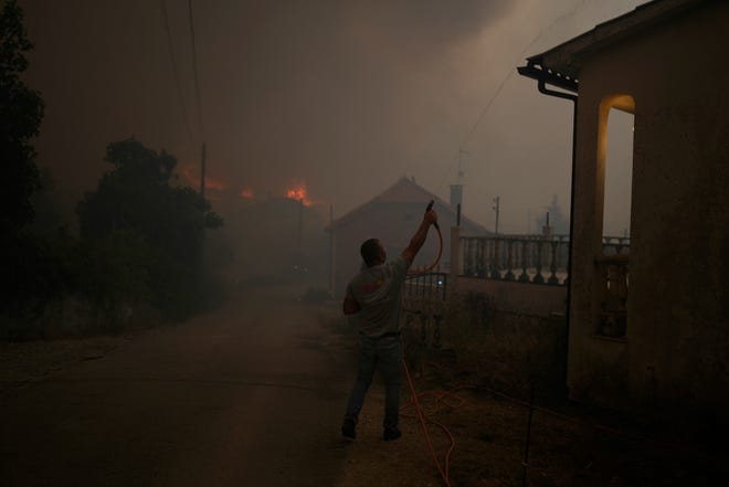 Un hombre usa una manguera de jardín para regar el techo de una casa mientras el humo de los incendios forestales oscurece el cielo en el pueblo de Bembosta, cerca de Anciao, en el centro de Portugal, el miércoles 13 de julio de 2022. Miles de bomberos en Portugal continúan combatiendo incendios en todo el país. país que han obligado a decenas a evacuar sus hogares.