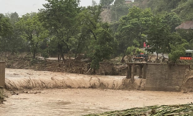 Un automóvil se encuentra junto a una sección de un puente que fue arrastrado por las aguas de la inundación en Qingyang, noroeste de China.