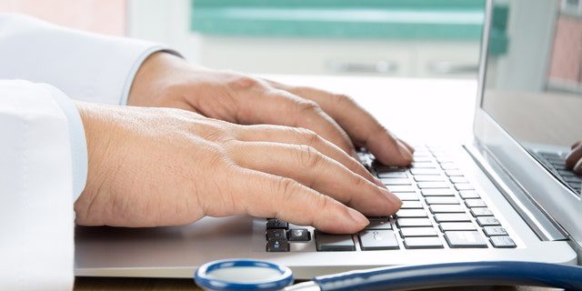 Primer plano de la mano de un médico escribiendo en una computadora